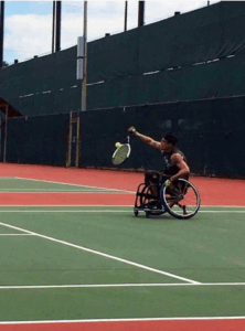 Man plays wheelchair tennis on green and red court. 